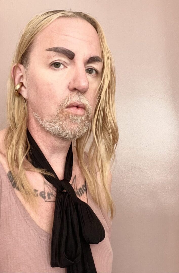 A man with long blonde hair and a black tie.