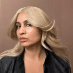 Person with long blonde hair, black jacket.