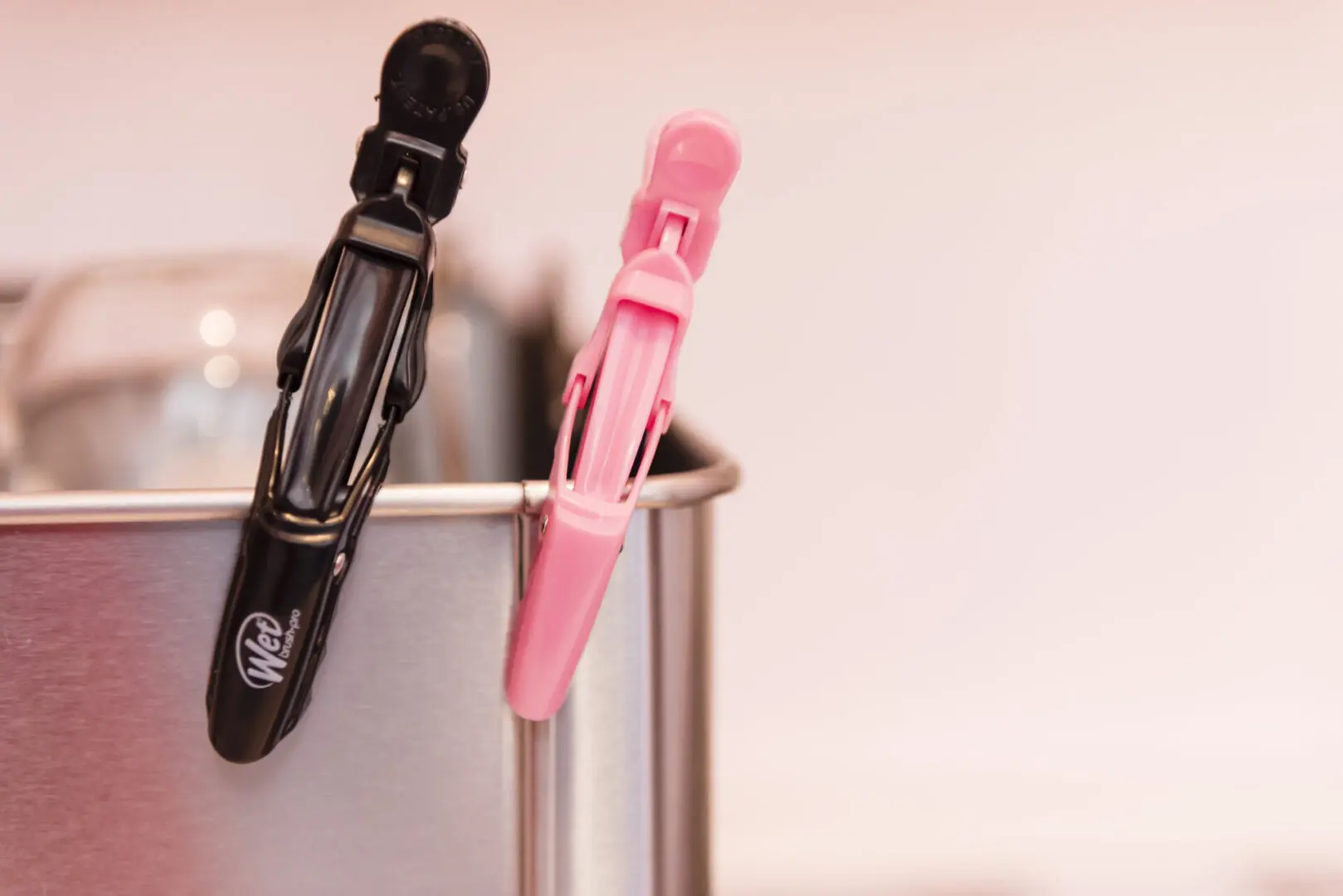 A pair of pink and black clothespins hanging on a metal holder.