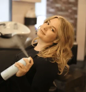A woman spraying hair with an air freshener.